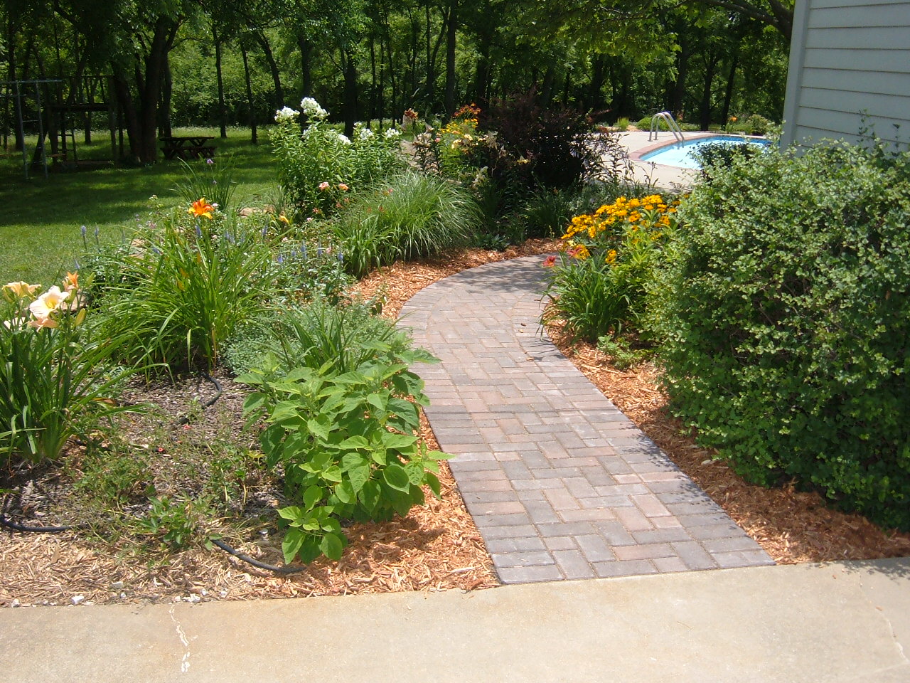 landscaped brick walkway approaching backyard pool
