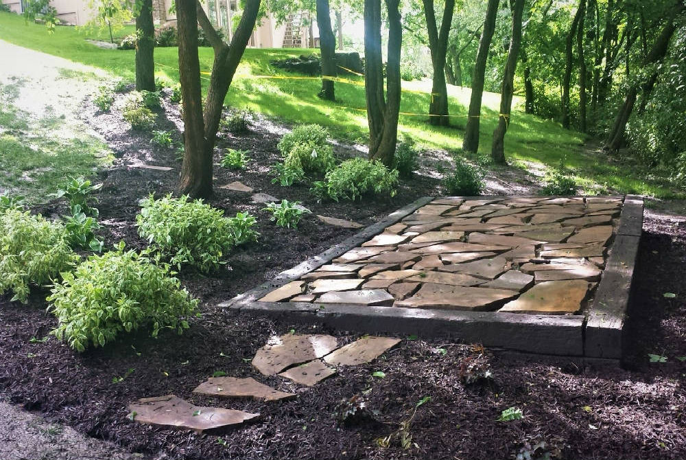 small stone patio framed with wood and mulch
