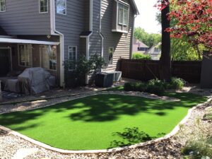 bright green lawn with rock landscaping, partially shaded by trees. Grey siding house also pictured.